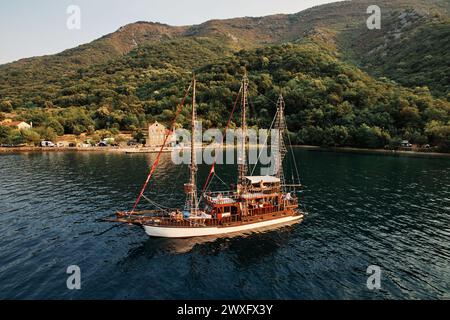 Sailboat with tourists sails along the bay against the backdrop of the mountain coast. Drone Stock Photo