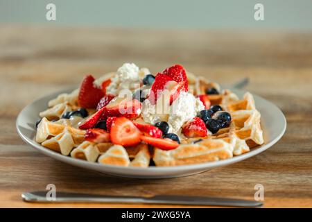 Golden Belgian Waffles topped with strawberries, blueberries, and freshly whipped cream. A mouthwatering delight in every bite for a special breakfast. Stock Photo