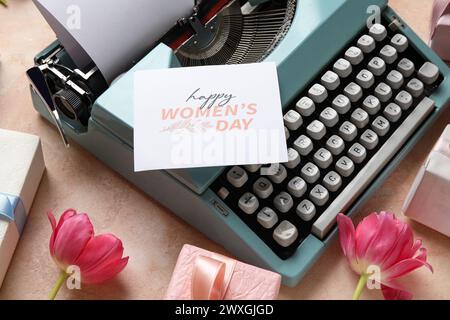 Festive postcard on typewriter for Women's Day, gift boxes and tulips on pink background Stock Photo