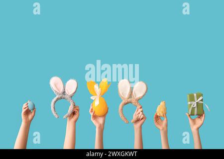 Female hands with chick, bunny ears headbands, painted egg and gift on blue background. Easter concept. Stock Photo