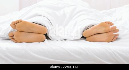 Couple's feet sticking out from under the covers in bed Stock Photo