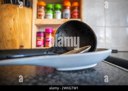 Soup leftovers on black plastic ladle on kitchen tabletop. Stock Photo