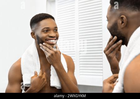 Man with towel patting face in bathroom mirror Stock Photo