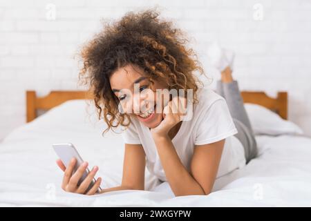 Curly-haired woman looking at phone in bed Stock Photo