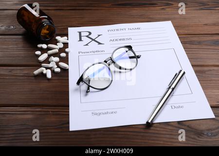 Medical prescription form with empty fields, glasses, pills and pen on wooden table Stock Photo