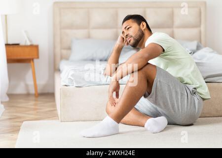 Black man sitting cross-legged on carpet beside bed Stock Photo