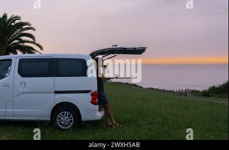 Man having a coffee at dawn leaning on his camper van in nature Stock Photo