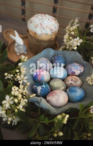 Top view of beautiful marbled Easter eggs with cosmic patterns in a blue fabric bowl surrounded by white spring flowers. Stock Photo