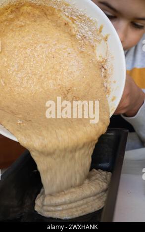 Child pouring the dough of a sponge cake into the baking pan Stock Photo