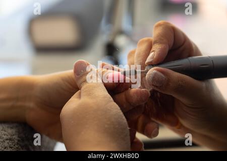 Woman in a beauty center doing the manicure to another woman with an electric filing Stock Photo