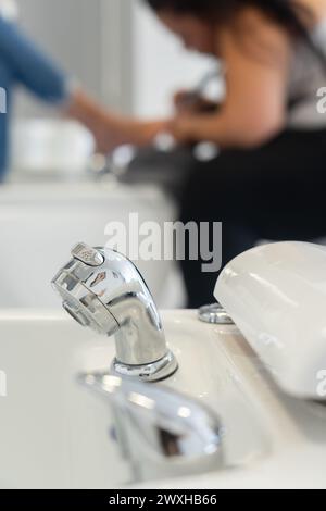 Faucet of a pedicure bathtub seen up close, with a woman doing the pedicure in the background Stock Photo