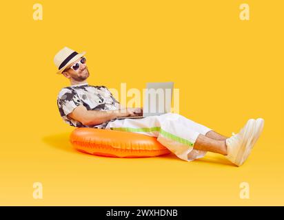 Happy businessman working on laptop while relaxing on swim ring during summer vacation Stock Photo