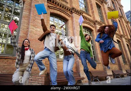 Happy group of multiethnic students celebrating the last day of school, jumping and raising arms. Stock Photo