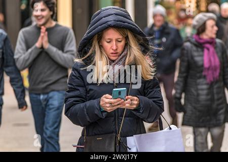 A woman multitasks, typing a text message while walking towards the camera through the streets of Dublin, Ireland. Stock Photo