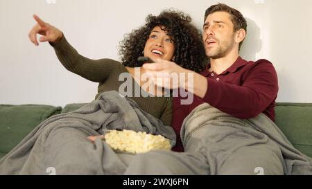 Multi-ethnic couple switching channel on tv with remote control Stock Photo