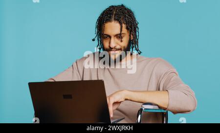Middle Eastern man composing email, typing on laptop keyboard, struggling to think of what to write. BIPOC person sending mail online, brainstorming message idea, studio background, camera B Stock Photo