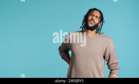 Hurt Middle Eastern man screaming from pain, suffering from back injury, having health problems. Injured BIPOC person feeling uncomfortable ache, yelling, studio background, camera A Stock Photo