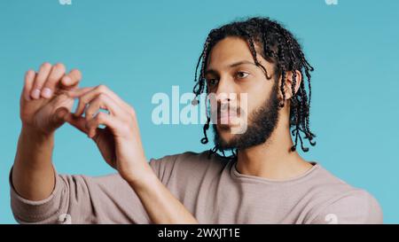 Happy person using augmented reality technology, doing swiping motions. BIPOC man using futuristic AR tech, making pinching zooming gesturing, blue studio background, camera B close up Stock Photo