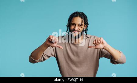 Upset Middle Eastern man showing thumbs down sign gesturing, disapproving, offering negative feedback. Disappointed BIPOC person doing rejection hand gesture, studio background, camera A Stock Photo