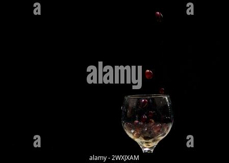 Red grapes falling into a clear glass goblet. Isolated on black background. Stock Photo