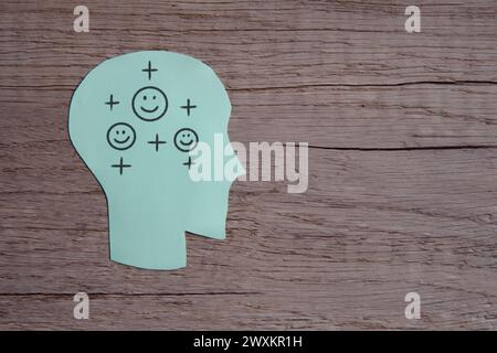 A green paper cut-out of a human head with a smile face and positive icon. Copy space for text. Positive thinking concept. Stock Photo