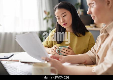 Selective focus shot of two ethnically diverse female college students sitting at table at home preparing for exam Stock Photo