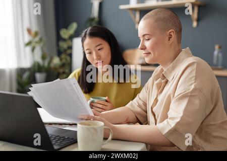 Selective focus shot of two ethnically diverse young female students sitting at table at home doing homework Stock Photo