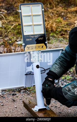 Assembly of fully autonomous, standalone LED street lighting, construction worker install support bracket to wooden pilon. Stock Photo