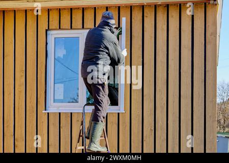 Roofing contractor installs exterior metal slopes on window while standing on stepladder on fall day. Stock Photo