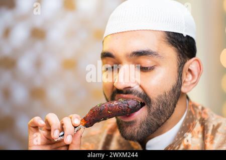 Close up head shot of muslim man eating chicken leg piece during ramadan festival feast Stock Photo