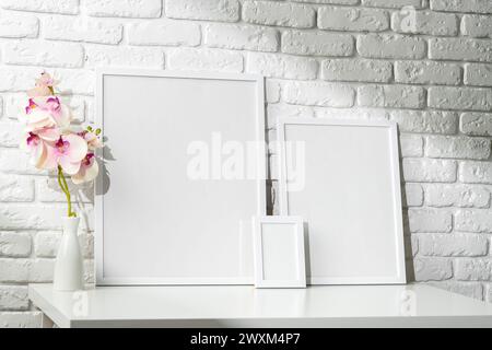 Three Blank Photo Frames on a White Table Against a Brick Wall Background Stock Photo