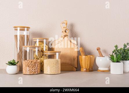 A set of glass jars with bulk products, cutting boards, , potted plants on kitchen countertop. Eco-friendly materials. Eco tableware. Front view. Stock Photo