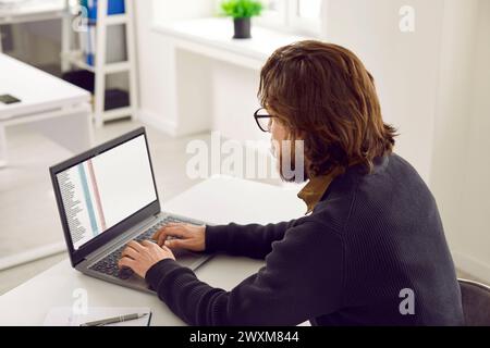 Man sitting at his office desk and working with files on a modern laptop computer Stock Photo