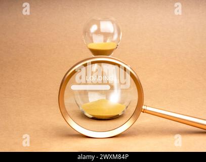 Loading update concept. Text "Loading..." on golden hourglass in magnifying glass lens on brown recycle paper background, minimal style. Setting a tim Stock Photo