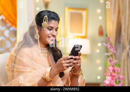 Happy indian muslim woman busy by using social media or watching videos on mobile phone in freetime at home - concept of technology,leisure activity Stock Photo