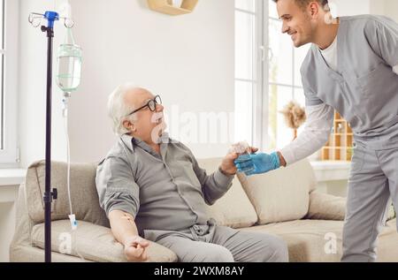 Young smiling male nurse taking care of old man with medical drop counter during procedure Stock Photo
