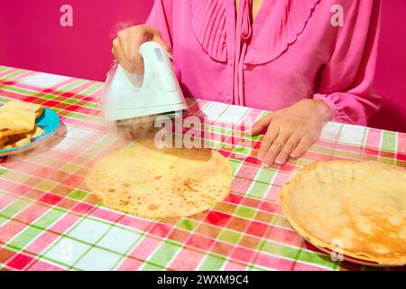 Woman in pink blouse ironing pancake on plaid tablecloth. Meme featuring unexpected ways to prepare food through humor. Stock Photo