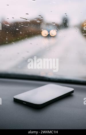 Smart phone on car dashboard on rainy day, selective focus Stock Photo