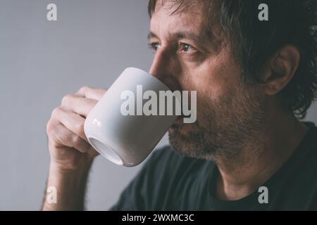 Unkempt man drinking morning coffee from a white mug, selective focus Stock Photo