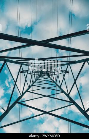 Electricity distribution tower from below, high voltage power lines under cloudy sky. Low angle view. Stock Photo