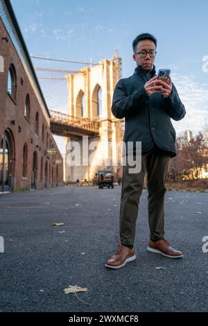 Focused Man Using Smartphone by the Iconic Brooklyn Bridge Stock Photo