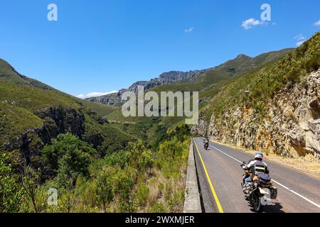 Two motorcyclists riding through the Tradouw scenic mountain road in South Africa surrounded by lush green hills and clear blue sky Stock Photo