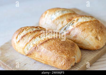 Two crusty golden brown bread loaves on wooden cutting board. Stock Photo