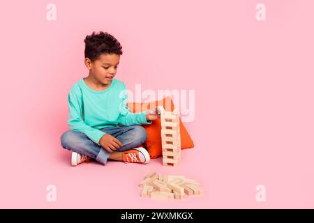 Full body photo of cute little boy play wooden blocks dressed stylish cyan clothes isolated on pink color background Stock Photo
