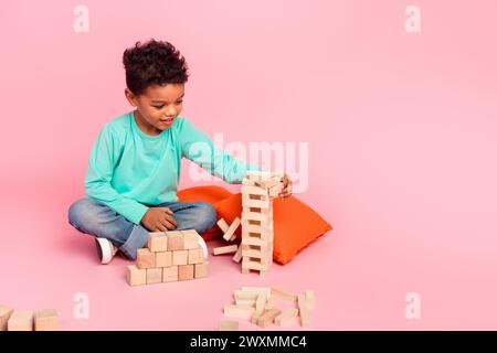 Full body photo of cute little boy play jenga wooden blocks game wear trendy aquamarine clothes isolated on pink color background Stock Photo