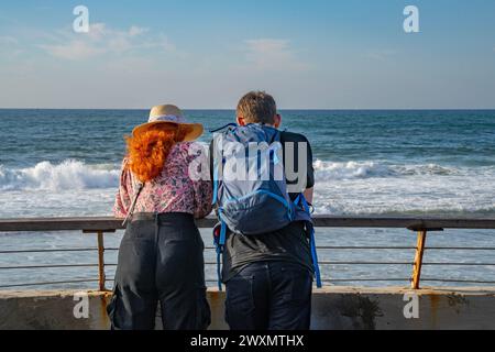 A man and a woman leaning on a railing at a port, looking at the sea on a clear sunny day. Stock Photo