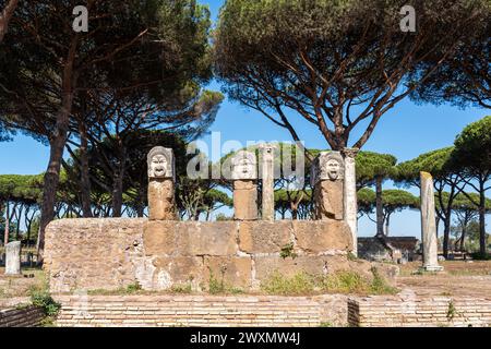 Theatrical male masks carved on marble blocks sustained by pillars in the ruins at the archaeological park in Ancient Ostia Stock Photo