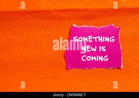 Something new is coming words written on pink torn paper piece with orange background. Conceptual symbol. Copy space. Stock Photo