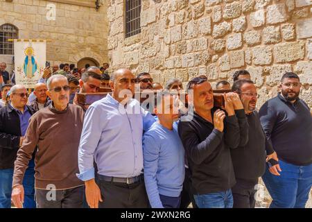 Jerusalem, Israel - March 29, 2024: Western good Friday scene in the yard of the church of the Holy Sepulchre, with pilgrim carrying cross and icons. Stock Photo