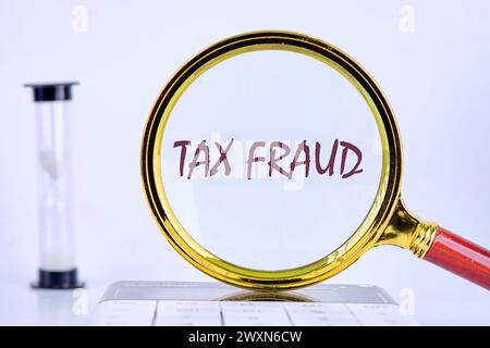 TAX FRAUD through a magnifying glass on a gray background next to an hourglass Stock Photo